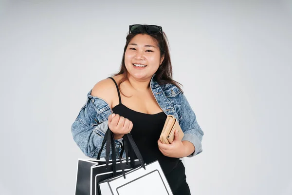 Portrait of fat woman in black dress and jeans jacket holding shopping paper bags isolate over white background.