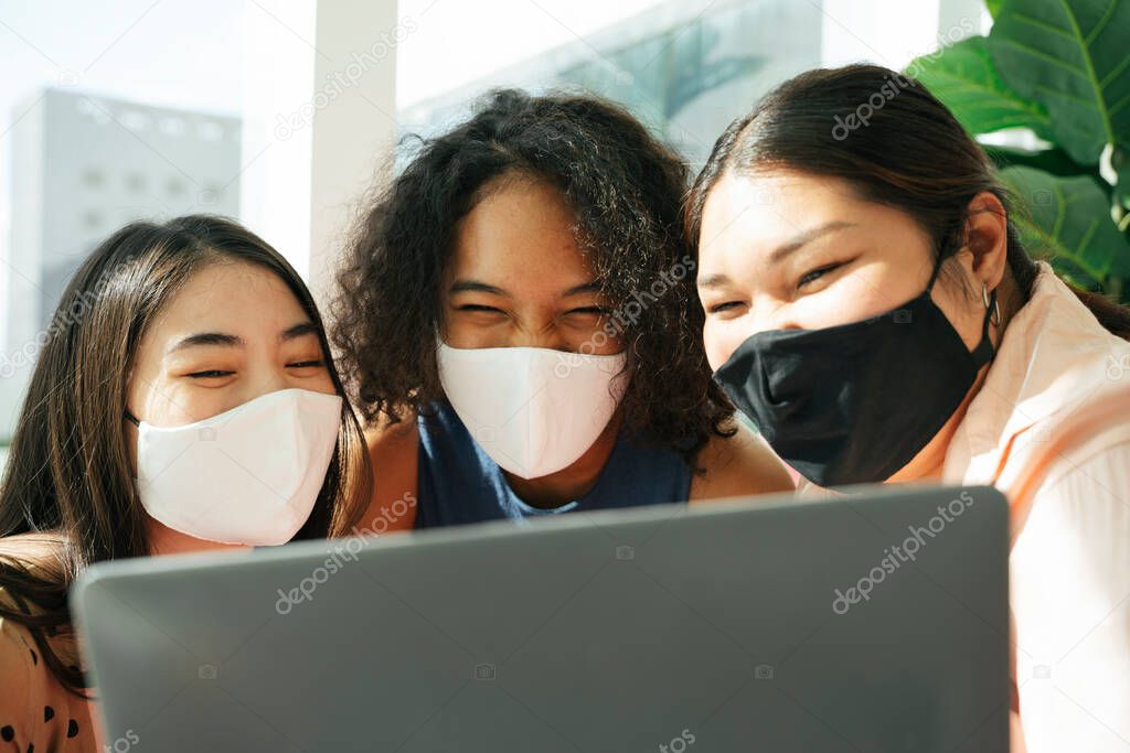 Diversity society concept. Asian and african women wearing mask doing video live stream with laptop together.