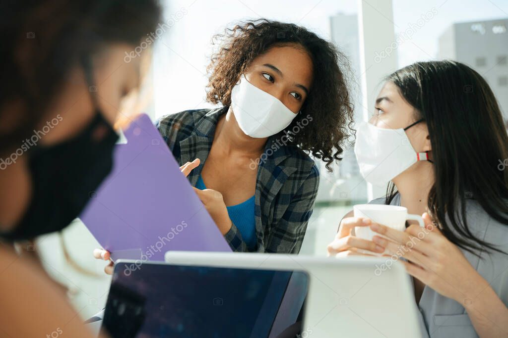 Group of three diverse asian and african business women wear mask working in office together.