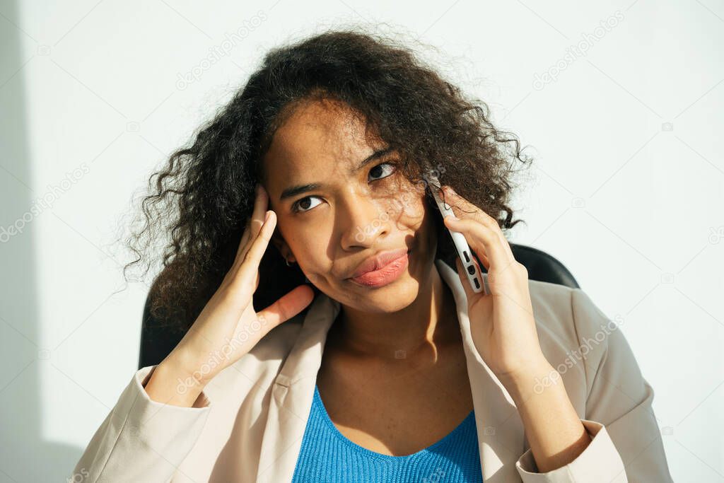 Close up portrait of stressful african curly hairstyle woman talking on the phone. Migraine and headache expression.