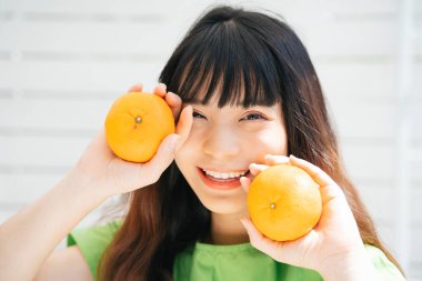 Elinde iki portakal tutan yeşil tişörtlü Asyalı genç bir gezginin portresi..