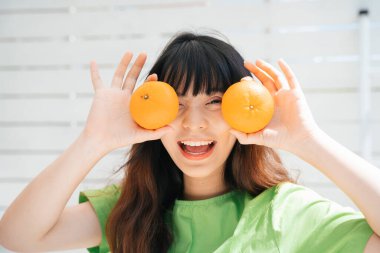 Elinde iki portakal tutan yeşil tişörtlü Asyalı genç bir gezginin portresi..