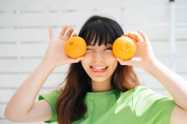 Elinde iki portakal tutan yeşil tişörtlü Asyalı genç bir gezginin portresi..