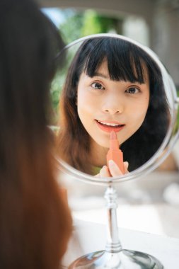 Masa aynasına ruj süren Asyalı genç bir kadın..