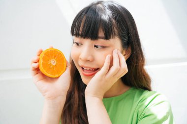 Elinde portakal dilimi olan yeşil tişörtlü Asyalı bir kadının portresi..