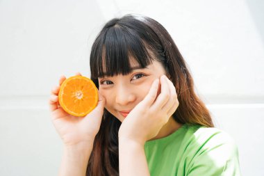 Elinde portakal dilimi olan yeşil tişörtlü Asyalı bir kadının portresi..