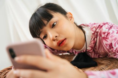 Pembe tişörtlü sıkılmış Asyalı bir kadın akıllı telefon kullanarak arkadaşıyla sohbet ediyor. Üzgün ifade görünümü.