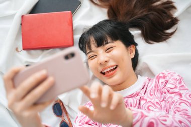 Üst Manzara - Pembe tişörtlü genç Asyalı kadın yatakta akıllı telefon kullanmaktan hoşlanıyor.