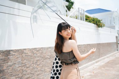 Genç Asyalı kadın gezgin şeffaf şemsiyeyle şehirde yürüyor..
