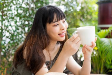Bahçede elinde bir fincan kahve tutan Asyalı genç bir kadın..