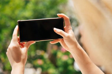 Gezgin kadın tatil köyünde açık havada akıllı telefon kullanıyor. Reklam için boş alan.