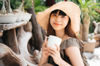 Avluda elinde kahve tutan Asyalı genç bir kadın..