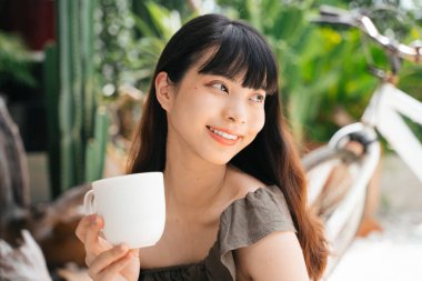 Bahçede elinde bir fincan kahve tutan neşeli Asyalı kadın..