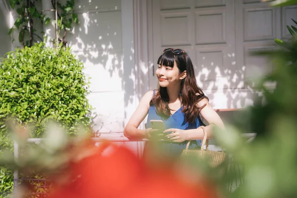 Cheerful happy young asian woman traveler wearing blue dress booking hotel or order stuff with online service with smartphone.