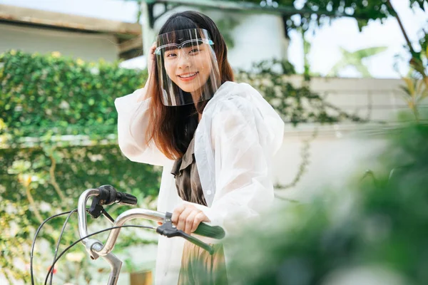 在公园外 年轻的亚洲女人穿着白色雨衣 戴着护目镜骑自行车 — 图库照片