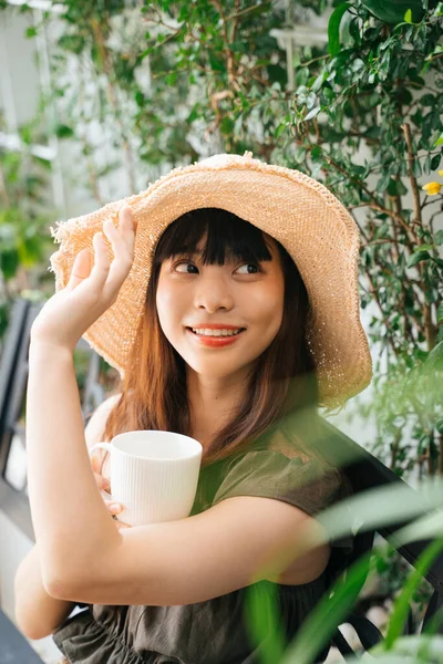 若いですアジアの女性を身に着けていますわら帽子保持カップのコーヒーで庭屋外 — ストック写真