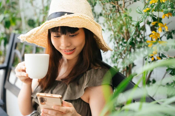 Jovem Mulher Asiática Usando Chapéu Bebendo Café Usando Smartphone Quintal — Fotografia de Stock
