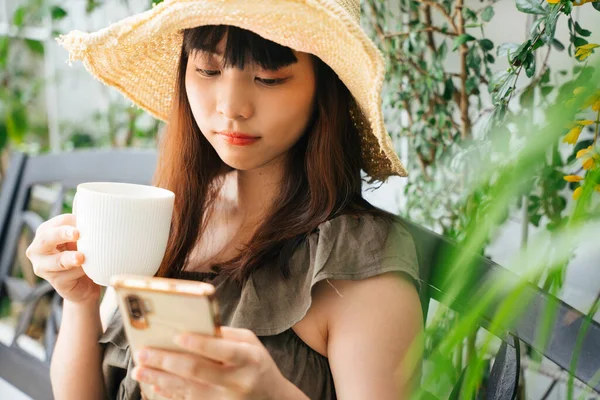 Jovem Mulher Asiática Usando Chapéu Bebendo Café Usando Smartphone Quintal — Fotografia de Stock