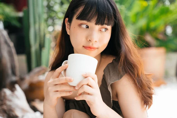 快乐的年轻亚洲女人在院子里端着一杯咖啡 — 图库照片