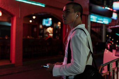 Dazlak adam gece şehirde yürürken kulaklık takıyor..