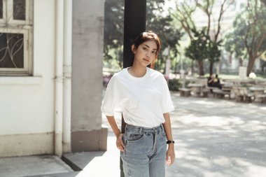 Sevimli bir kız direğe yaslanıyor, eli kalçasına dokunuyor ve çekici bir şekilde kameraya bakıyor..