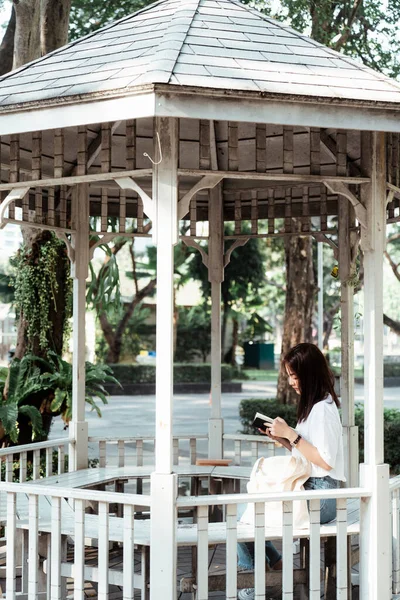 Cute girl in white t-shirt read lecture notebook in the pavilion at university park, long shot.