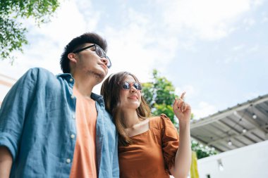 Şehirde yürüyen Asyalı çift güneş gözlüğü takıyor. İkisi de gökyüzüne bakıyor..