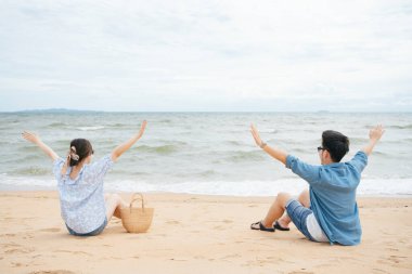 Sahilde oturan Asyalı çift, iki elini havaya kaldırdı. .