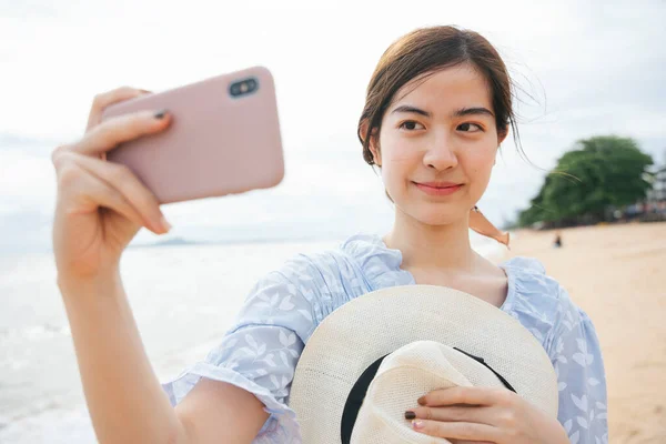 アジアのカップル旅行者と帽子をかぶってスマートフォンでビーチで自撮り — ストック写真