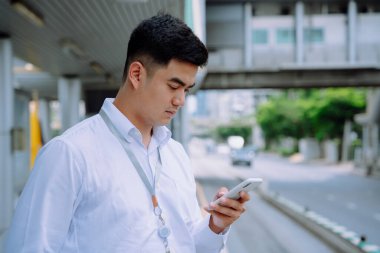 Asyalı iş adamı kaldırımda otobüs beklerken akıllı telefon kullanıyor..