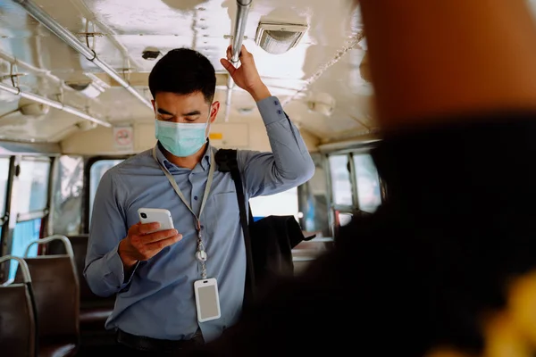 Asian business man wear mask using smartphone on a bus in Bangkok.
