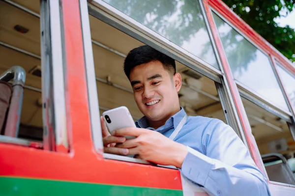 Cheerful asian man using smartphone on a bus in Bangkok.