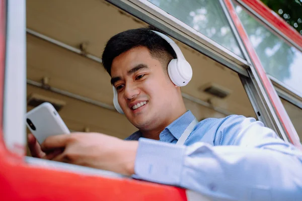 Cheerful asian man using smartphone listen to music with wireless headphone on a bus in Bangkok.