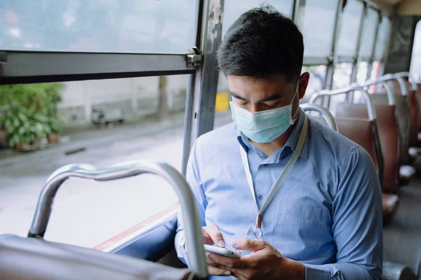 Asian business man wear mask using smartphone on a bus.