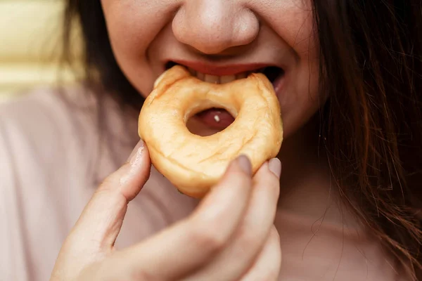 Cropped image of plain donut is bitten by the fat woman\'s mouth.