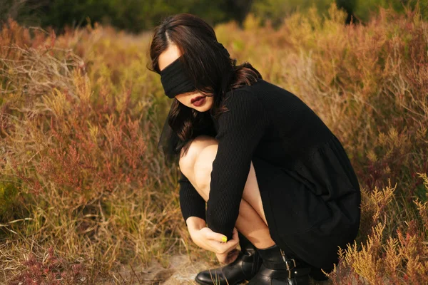 Black girl looking throughthe blindfold that cover her eyes, sitting at the field.