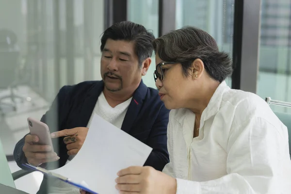 Old elderly senior business people working together in meeting room. They looking at candidate list on paper and make a call for interview.