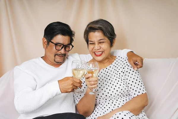 シニアアジアのカップル座っています上のソファお祝いでワイングラス — ストック写真