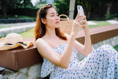 Parkta akıllı telefon kullanan Asyalı güzel bir gezgin kadın..