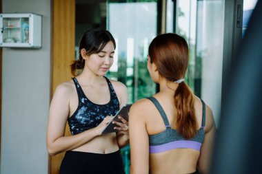 Güzel, sağlıklı bir kadın spor salonunda antrenörle egzersiz programı hakkında konuşuyor..