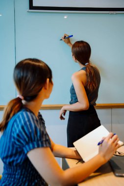 Asyalı iş kadını beyaz tahtaya rapor yazıyor.