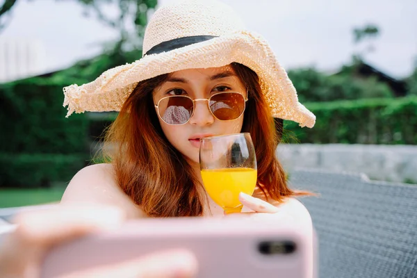 亚洲美女旅行者头戴帽子 戴着太阳镜 拿着橙汁自拍的近照 — 图库照片