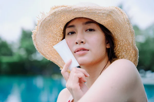 Close up - Beautiful asian woman traveler wear hat with cream sunblock lotion at swimming pool.