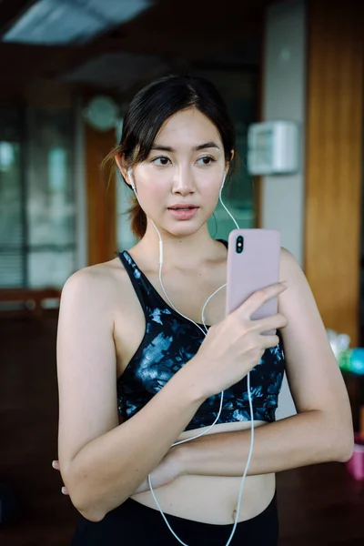 美丽健康的女人穿着运动胸罩 用耳机听音乐 她在用智能手机选歌 — 图库照片