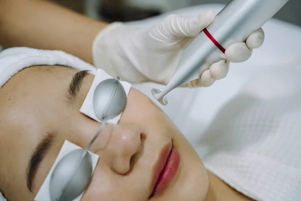 Asian woman getting laser and ultrasound face treatment in medical spa center.