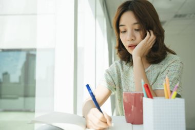 Sınıfta çalışan güzel Asyalı kadın portresi, kurşun kalemle bir kitaba bir şeyler yaz..