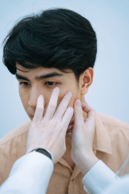 Güzellik uzmanı güzellik kliniğinde genç adamın yüzünü kontrol ediyor..