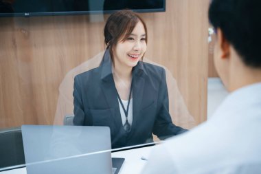 Güzel Asyalı resepsiyonist masanın arkasındaki müşteriye bilgi veriyor..