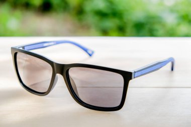 Yeşil arka plan ile masada mavi çizgili siyah güneş gözlüğü.