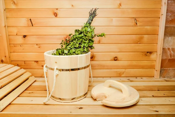 Rus saunası. Ahşap bir arka plan üzerinde ahşap bir kova içinde Huş süpürgesi.
